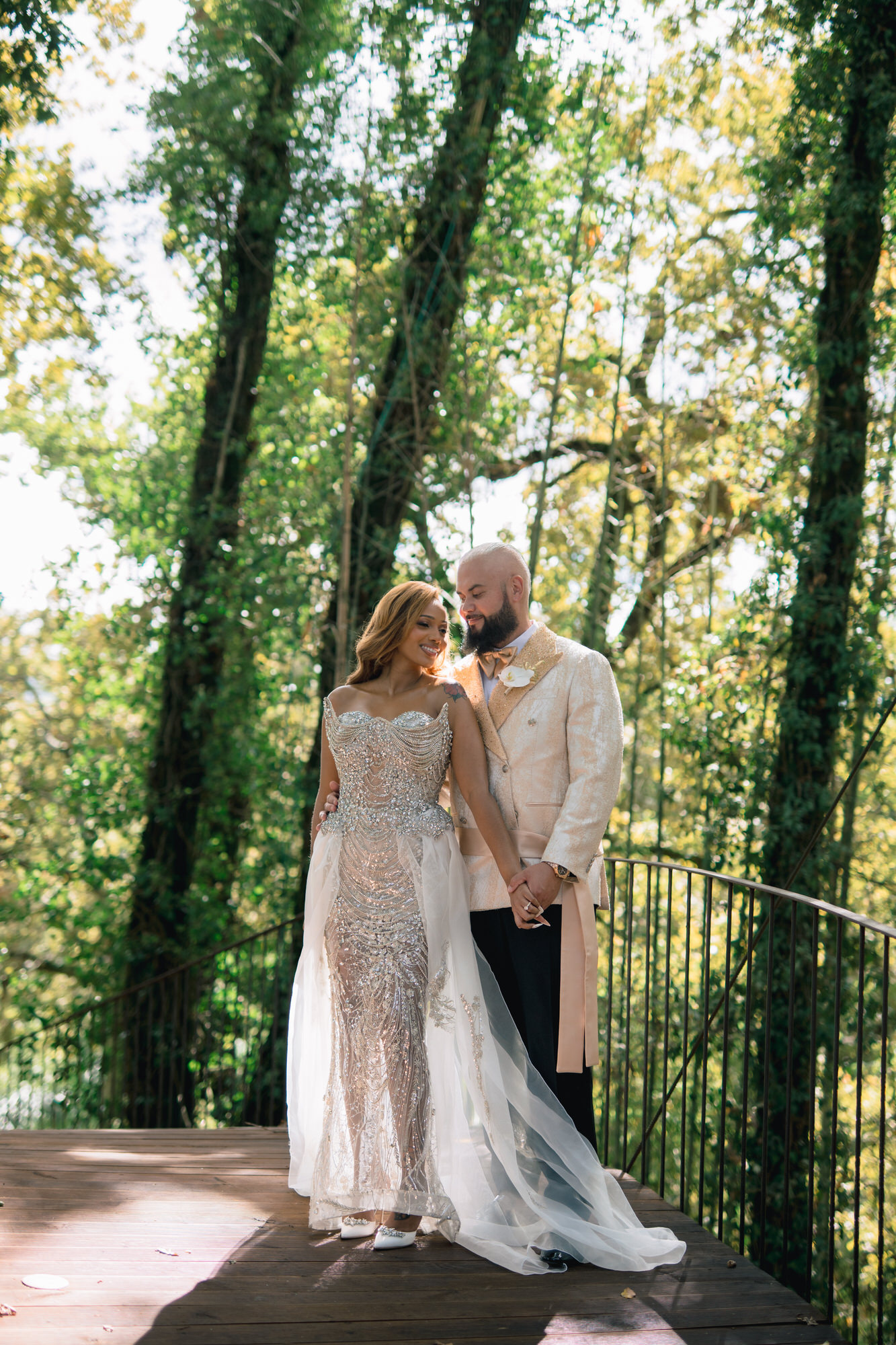 The couple embracing among tall trees, her gown shimmering in the dappled light