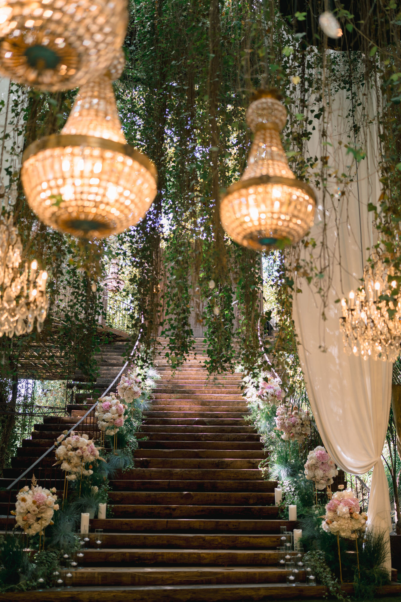 The ceremony aisle: a staircase lined with roses beneath crystal chandeliers and hanging greenery