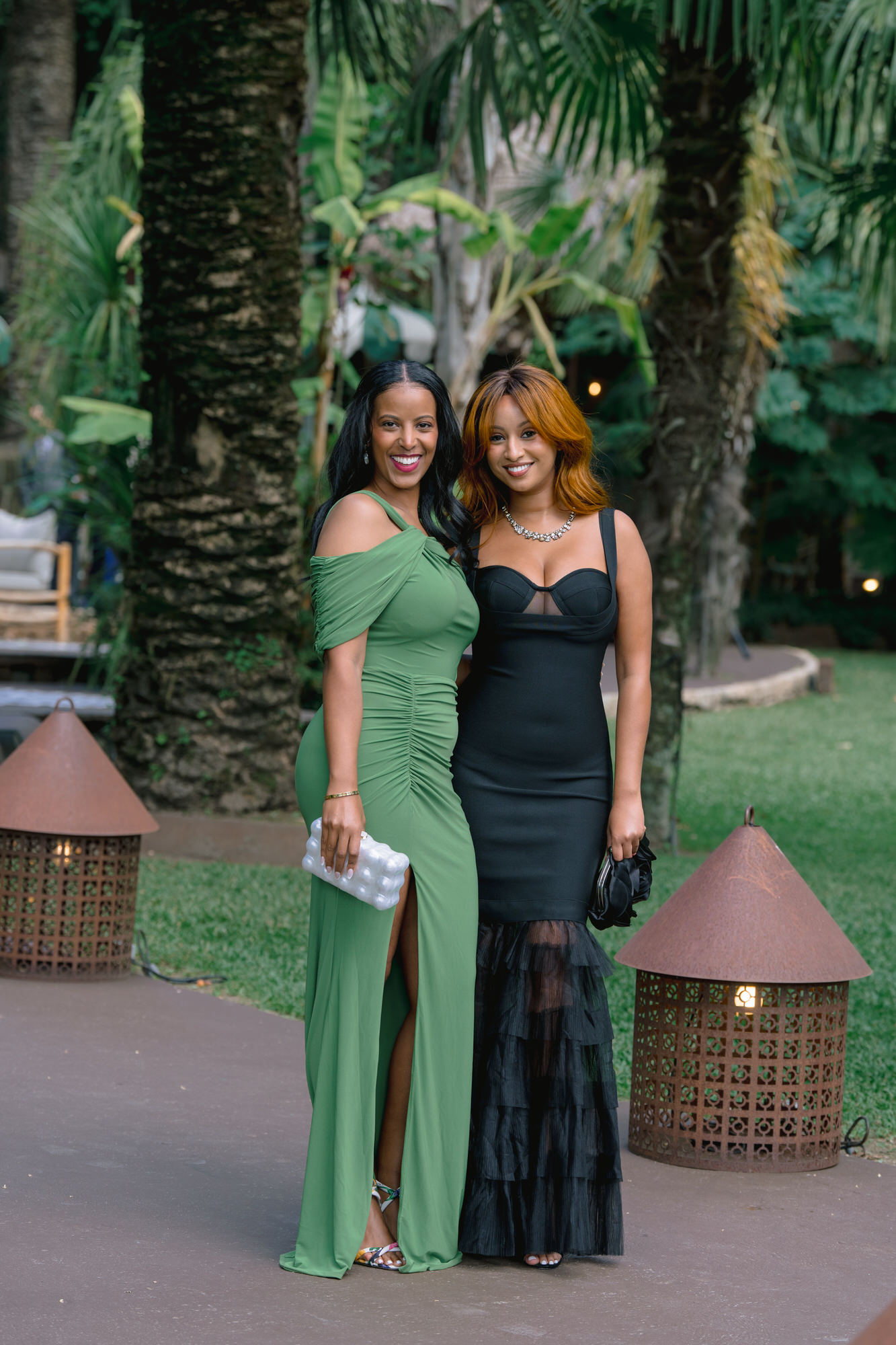 Two guests in a green dress and a black dress posing together on the lawn
