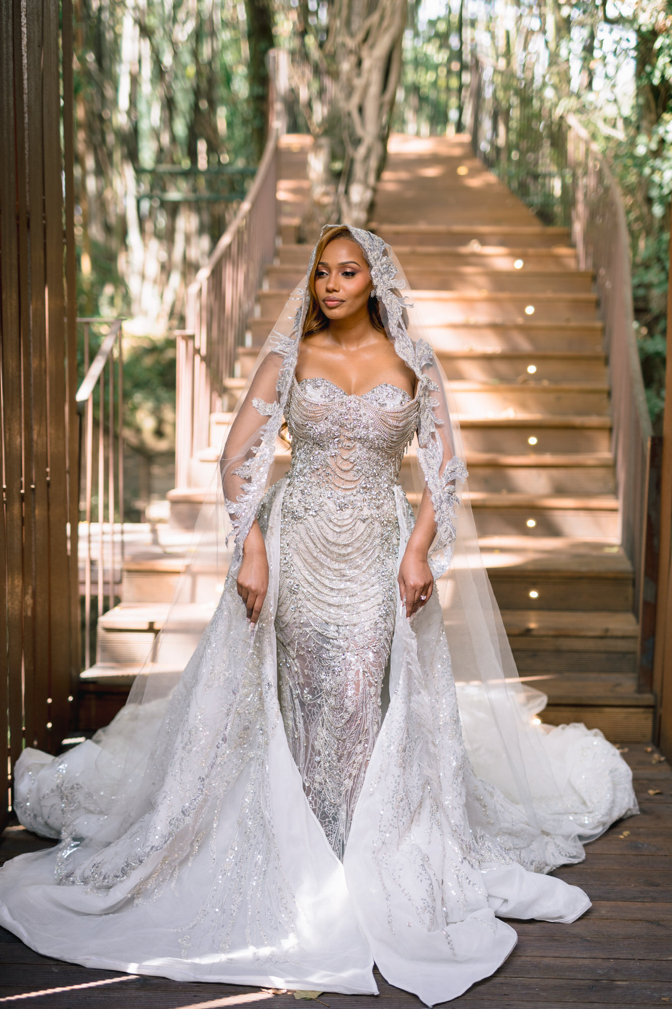 Close-up of the bride on the forest staircase, her veil and beaded overskirt trailing behind her