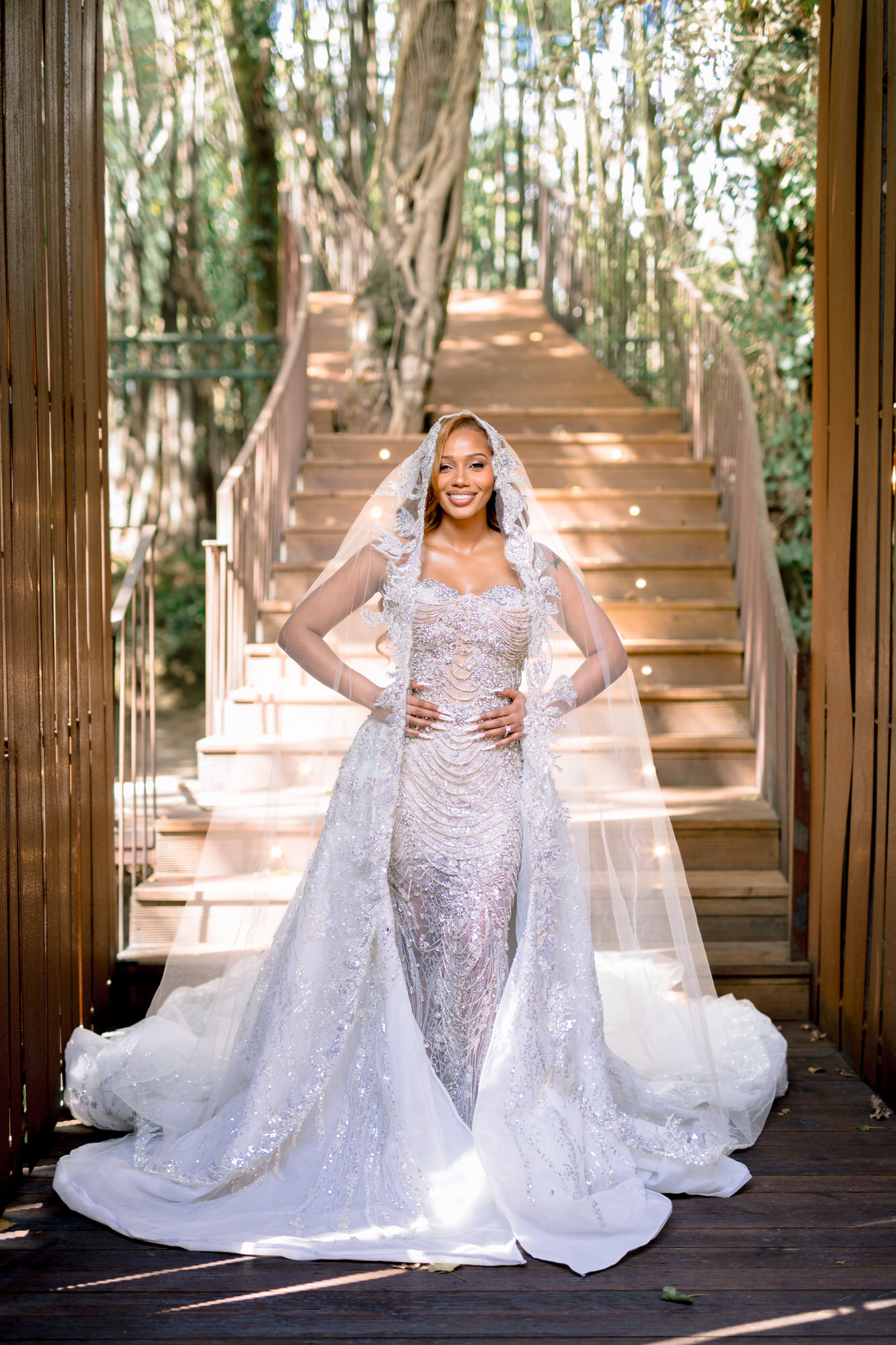 The bride in a beaded gown and long veil on a wooden staircase in the forest