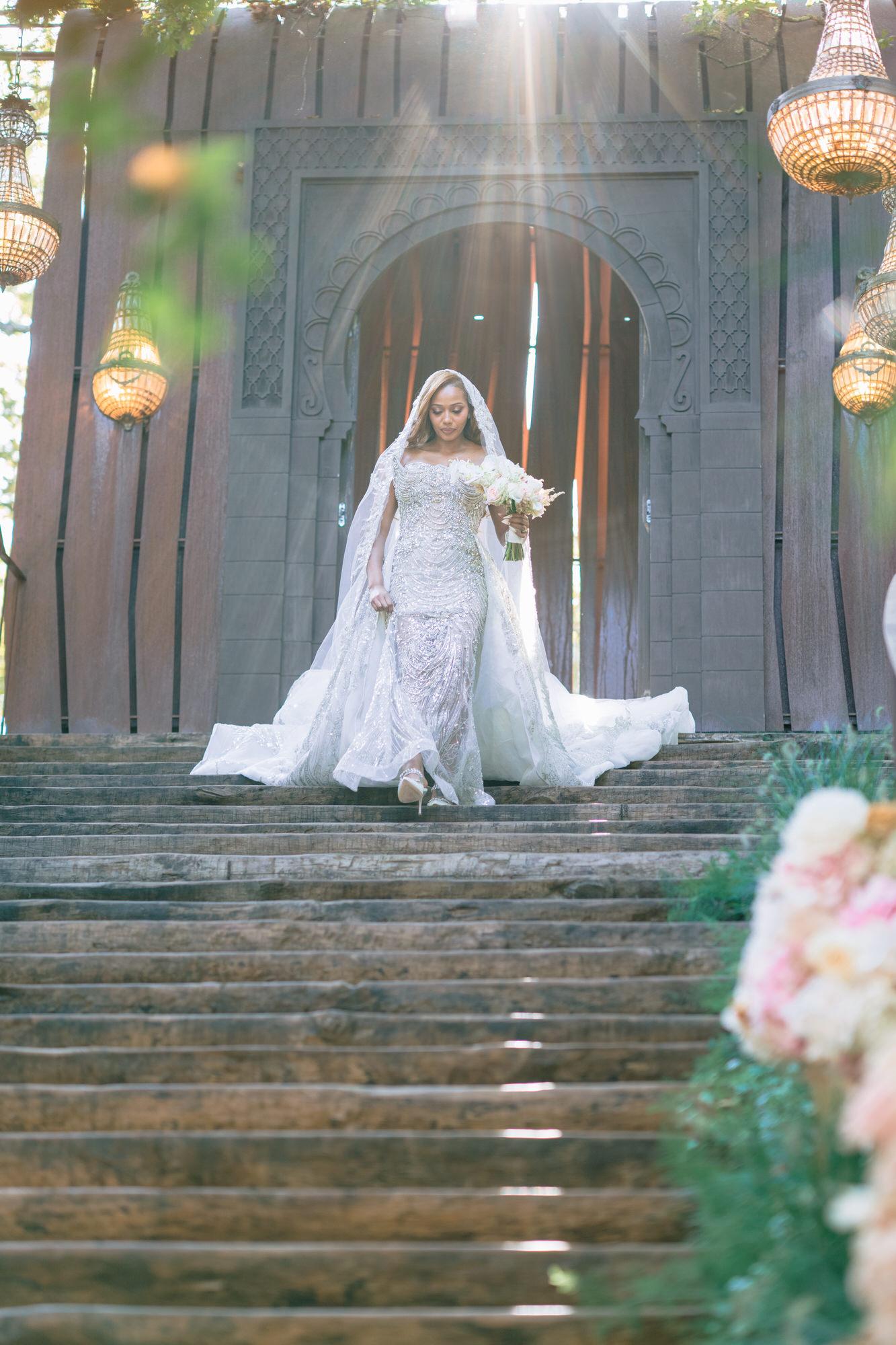 The bride at the top of the stone steps in a long veil, a tall wooden door behind her
