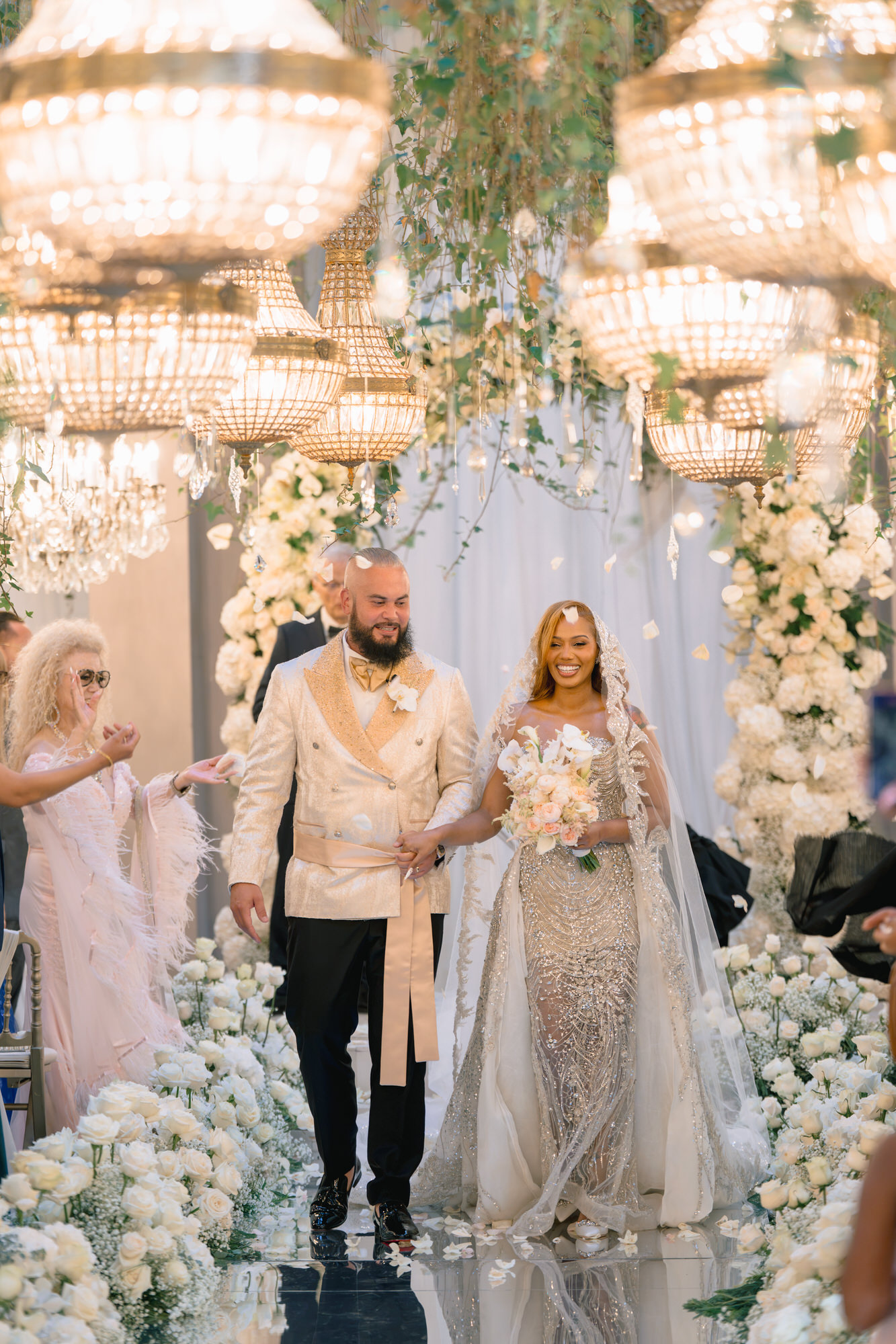 The newlyweds walking back up the aisle, he in a cream jacket and she holding her bouquet
