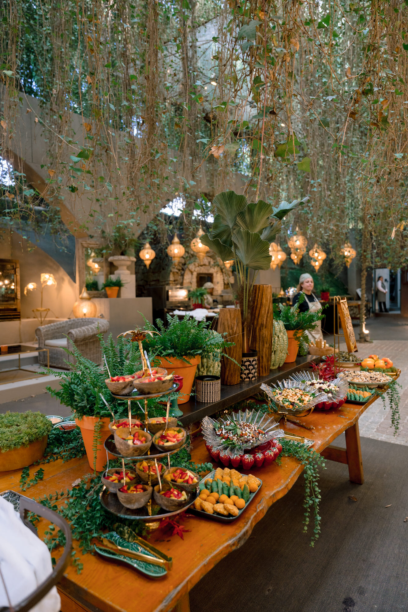 A grazing table of fresh produce on a wooden board beneath hanging branches