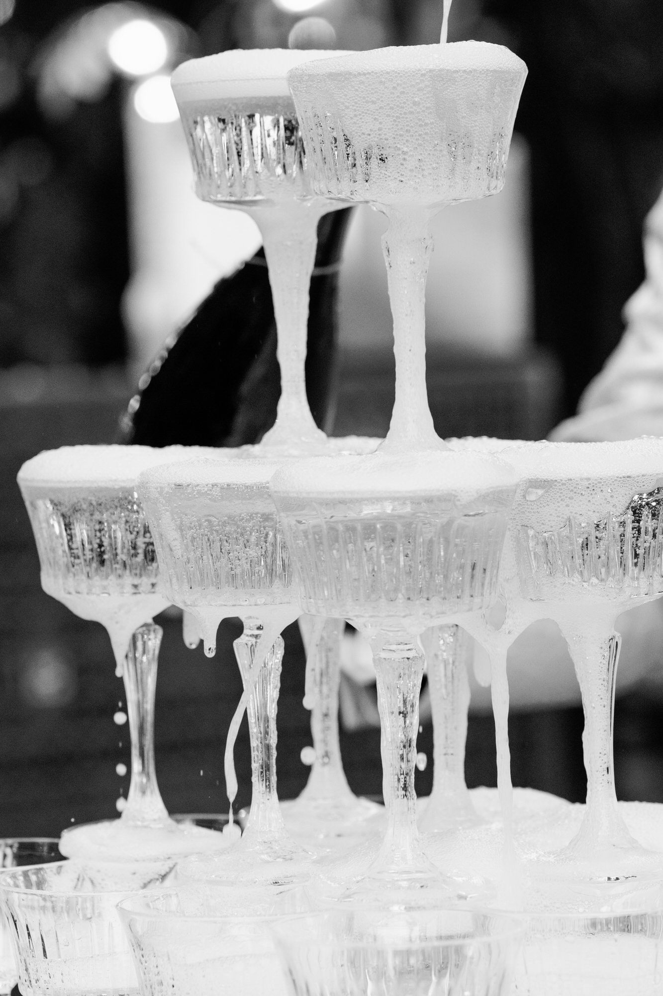 Black-and-white image of a champagne tower overflowing at the reception
